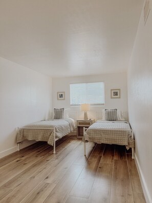 A bedroom with two single beds, a bedside table with a lamp, a window with blinds, and a framed picture on the wall. - Punta Gorda Waterfront Escape, Private Pool, Gulf Access, 3BR, Near Downtown (Punta Gorda)