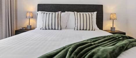 Una cama bien hecha con almohadas a rayas, cabecera oscura y manta verde.