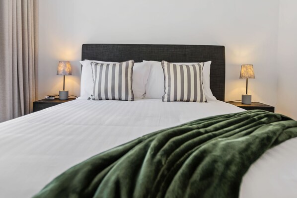 A neatly made bed with striped pillows, a dark headboard, and a green blanket. - Tropical Koru Cottage - Private Pool - BBQ (Cairns)