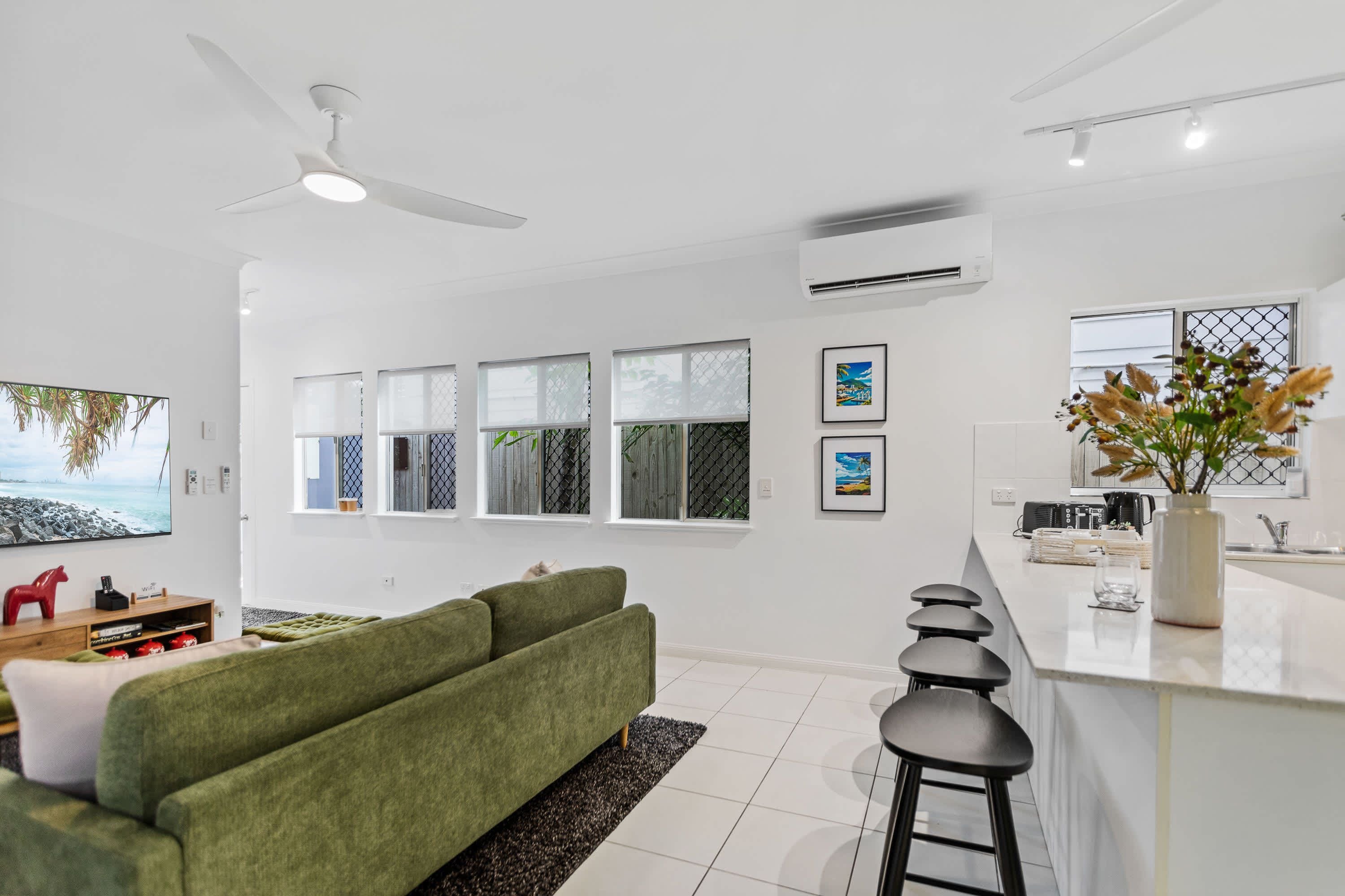 A modern kitchen with a bar area, white cabinetry, and a green sofa in the living area.