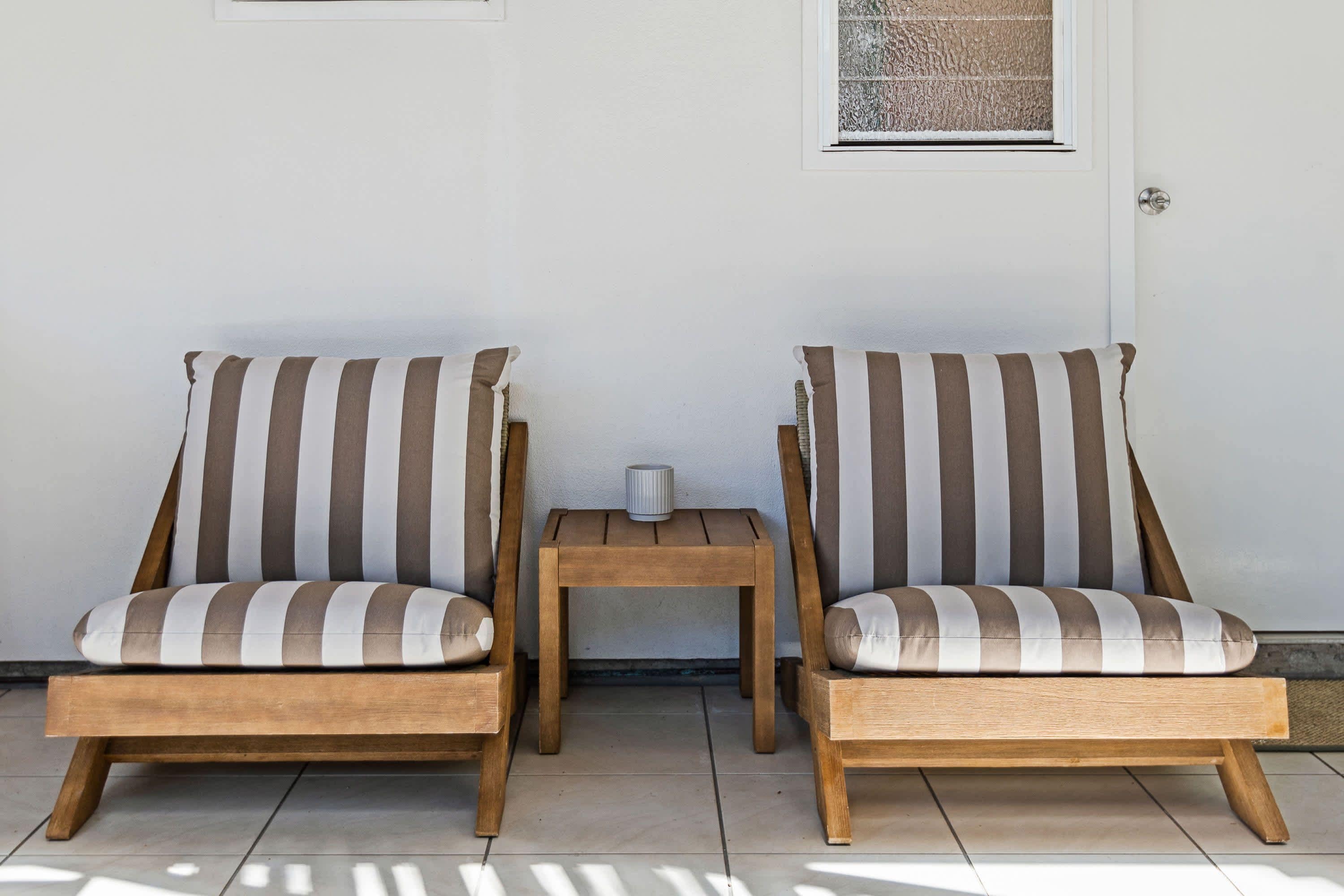 Two wooden chairs with striped cushions, a small wooden table, and a window with a textured pattern.