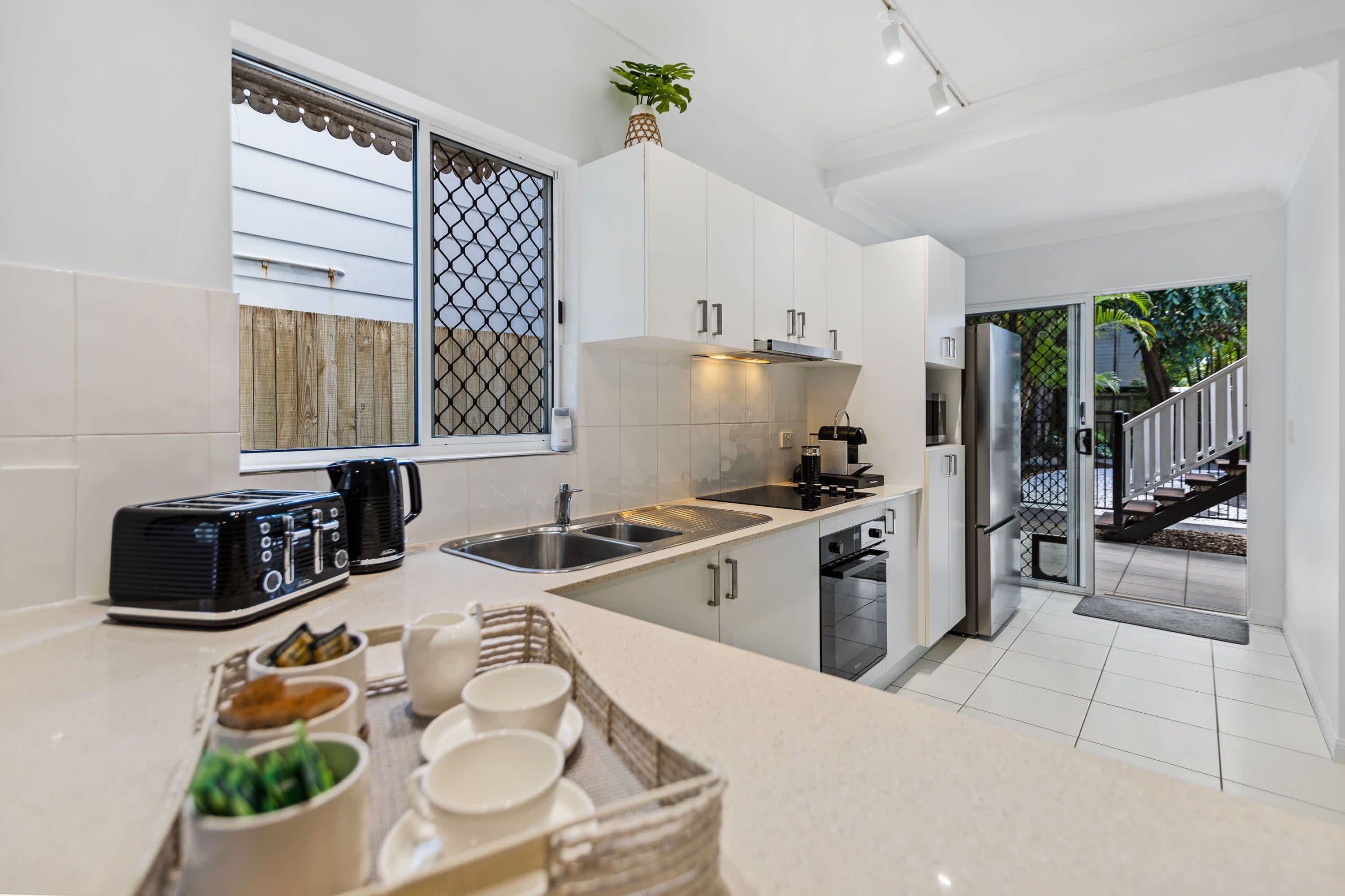 A modern kitchen with white cabinets, a stainless steel sink, and a built-in oven.