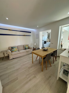 A modern living room with a sofa, a dining table, and a kitchen in the background. - House of Saint Lucy! With a View of the Ria Formosa! (Santa Luzia)