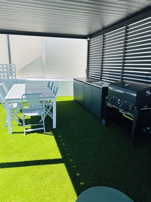 An outdoor patio with a table and chairs, a grill, and a wall with horizontal blinds. - House of Saint Lucy! With a View of the Ria Formosa! (Santa Luzia)