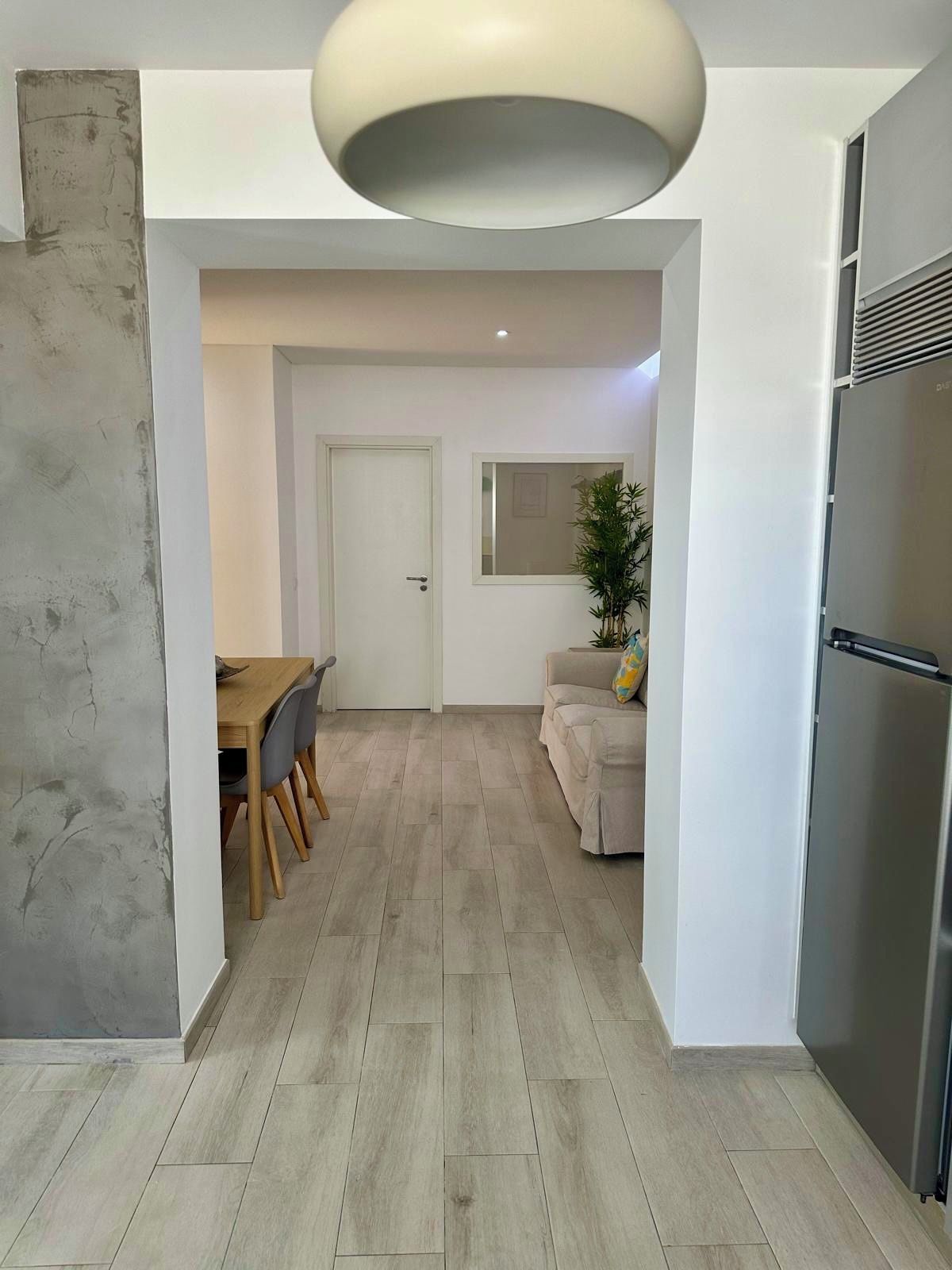 A modern kitchen with a built-in refrigerator, a dining area with a wooden table and chairs, and a hallway leading to a living space.