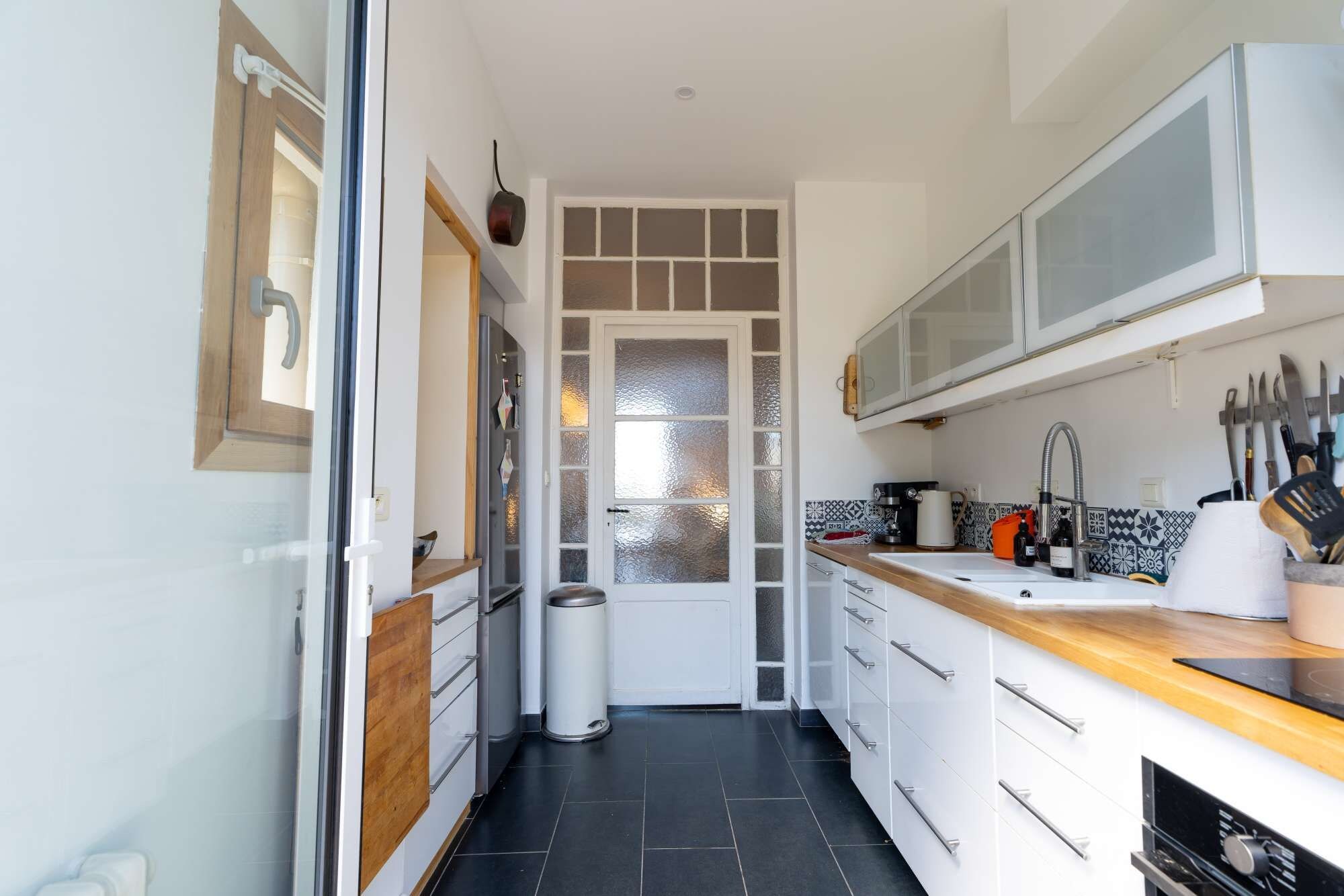 A modern kitchen with white cabinets, a wooden countertop, and a stainless steel sink.