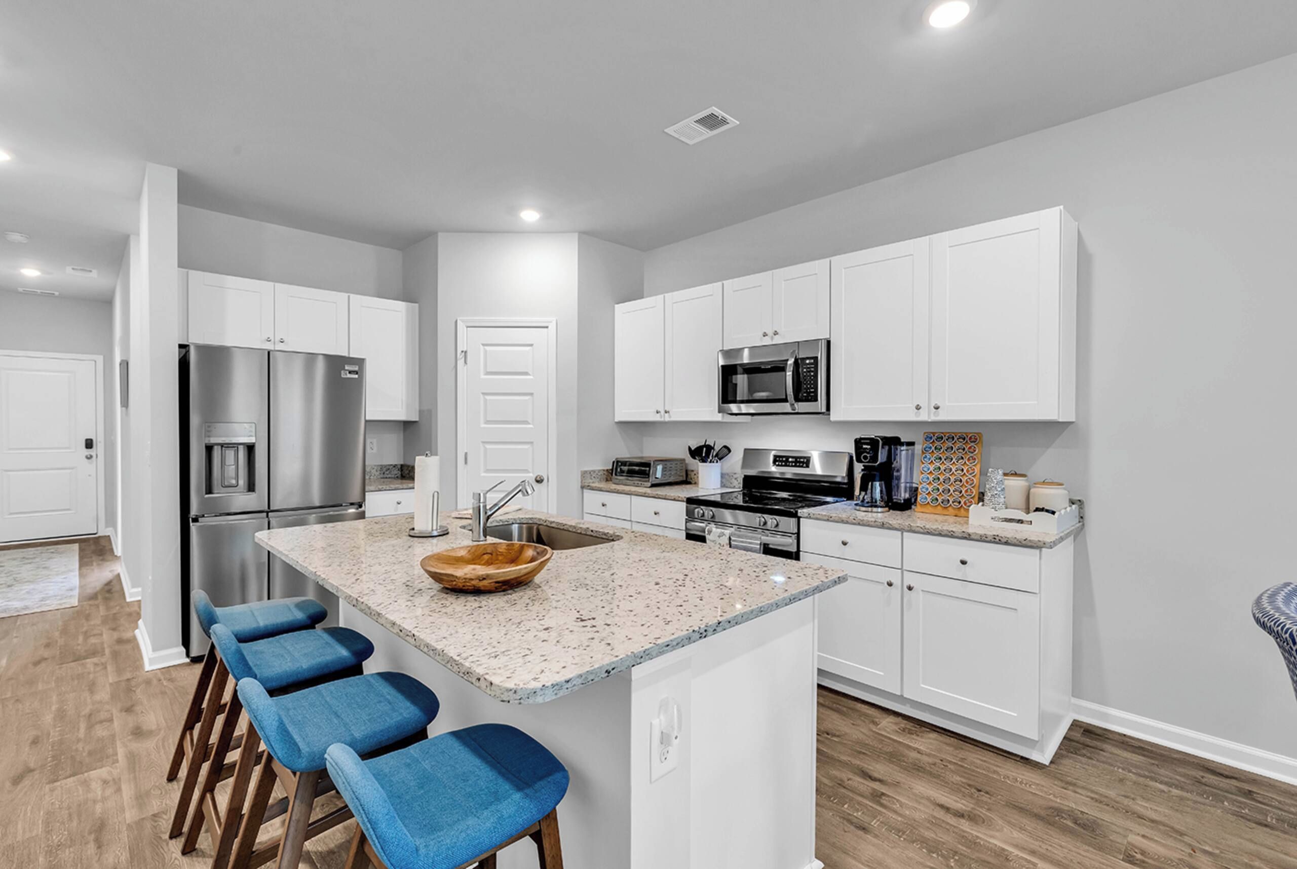 A modern kitchen with white cabinets, stainless steel appliances, a granite countertop, and a wooden bowl centerpiece.