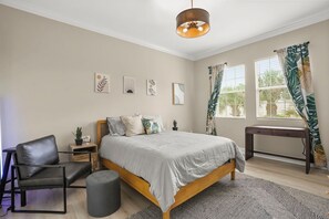 Een slaapkamer met een bed, een stoel, een bureau, een raam met gordijnen en decoratie aan de muur.