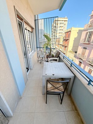 Uma varanda com mesa e cadeiras, um vaso de planta e vista para edifícios vizinhos.
