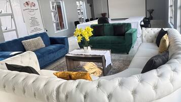 Een moderne woonkamer met een gebogen witte bank, een blauwe bank en een groene bank. Er staat een salontafel met een vaas vol gele bloemen.
