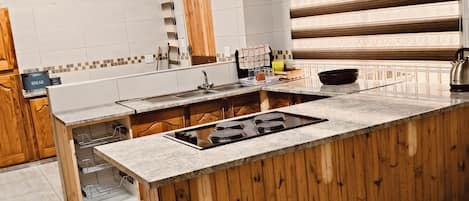 A kitchen with a wooden island, white tiled backsplash, and a large window with blinds.