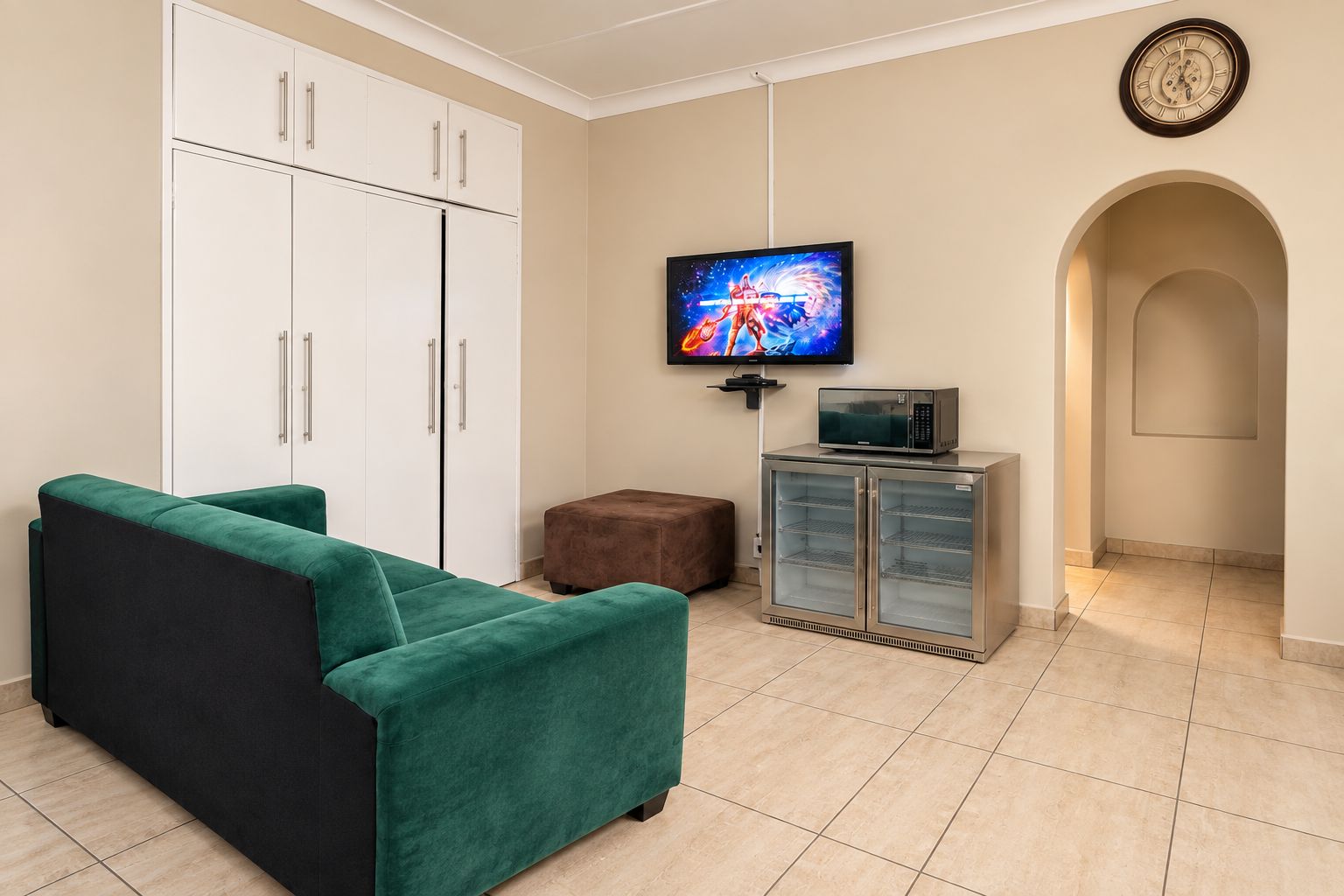A living room with a green sofa, a television, a microwave, and a refrigerator.