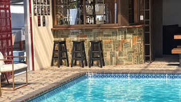 A poolside bar with stools and a sign above it.