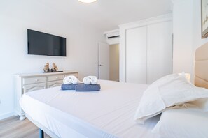 Une chambre d’hôtel avec un grand lit, un téléviseur à écran plat fixé au mur, une commode avec un miroir et une porte donnant sur une autre pièce.