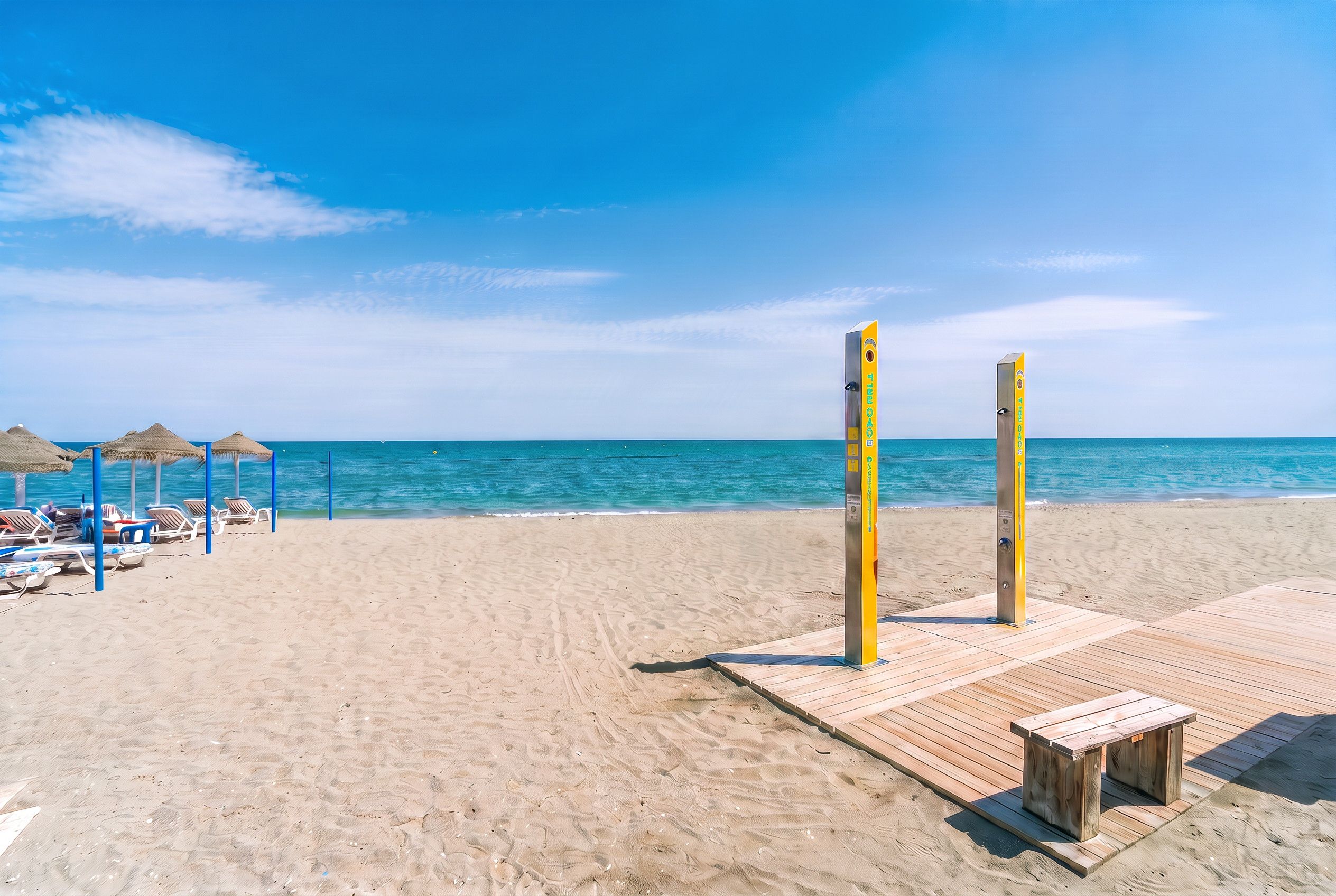 Una playa con tumbonas y sombrillas, una terraza de madera y dos postes altos con texto.