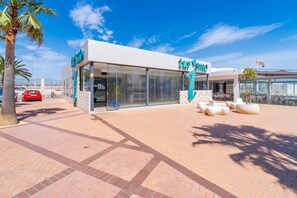 A modern building with a glass facade, palm trees, and a red car parked in front. - Cubo's Suite Mar Fuengirola Apartment / center / air conditioning / terrace / free wifi (Fuengirola)