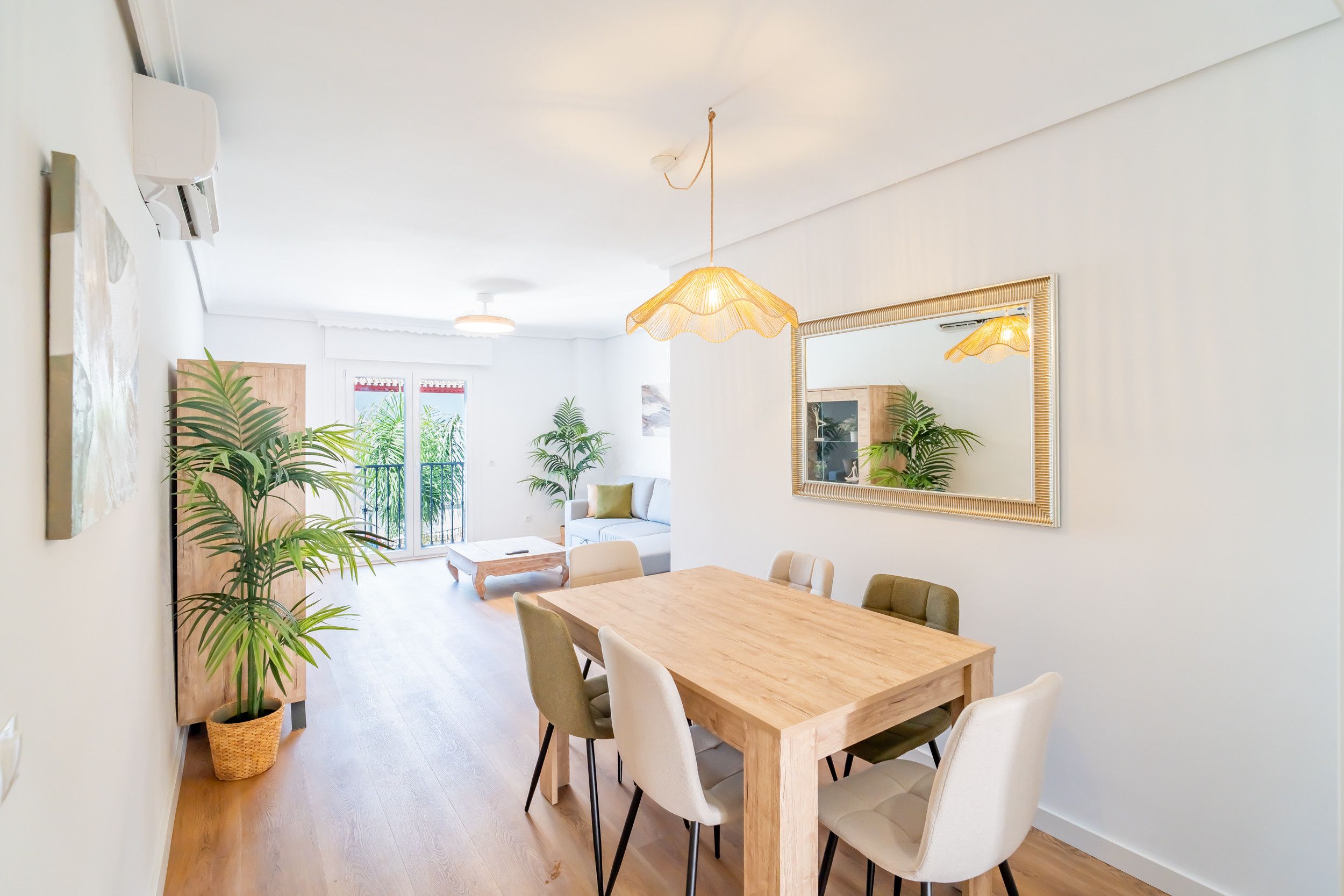 A modern dining area with a wooden table and chairs, a large mirror, and potted plants.