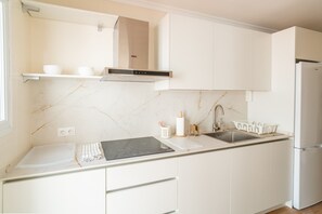 Eine moderne Küche mit weißen Schränken, einer schwarzen Induktionskochplatte, einer Edelstahl-Spüle und einem weißen Kühlschrank.