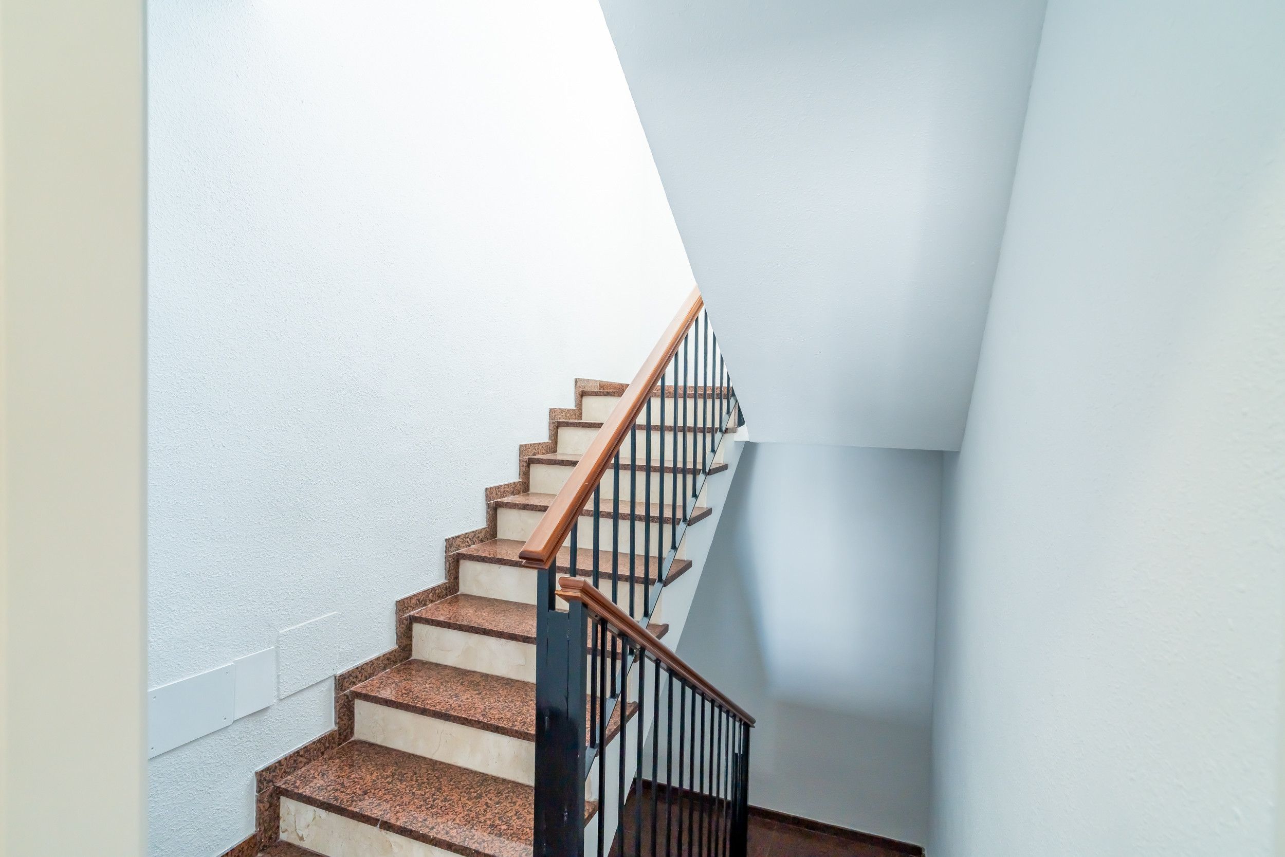 Una escalera con escalones de madera y barandales negros, que conduce a una plataforma con una pared blanca.