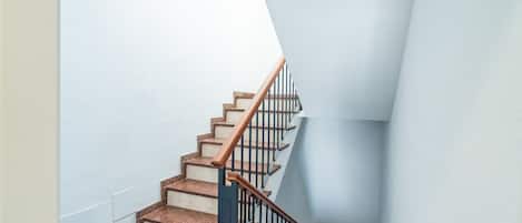 Una escalera con escalones de madera y barandales negros, que conduce a una plataforma con una pared blanca.