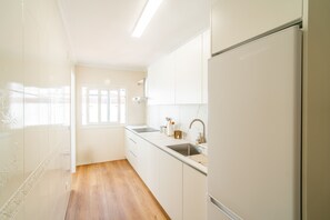 Een keuken met witte kastjes, een roestvrijstalen spoelbak en een houten vloer.