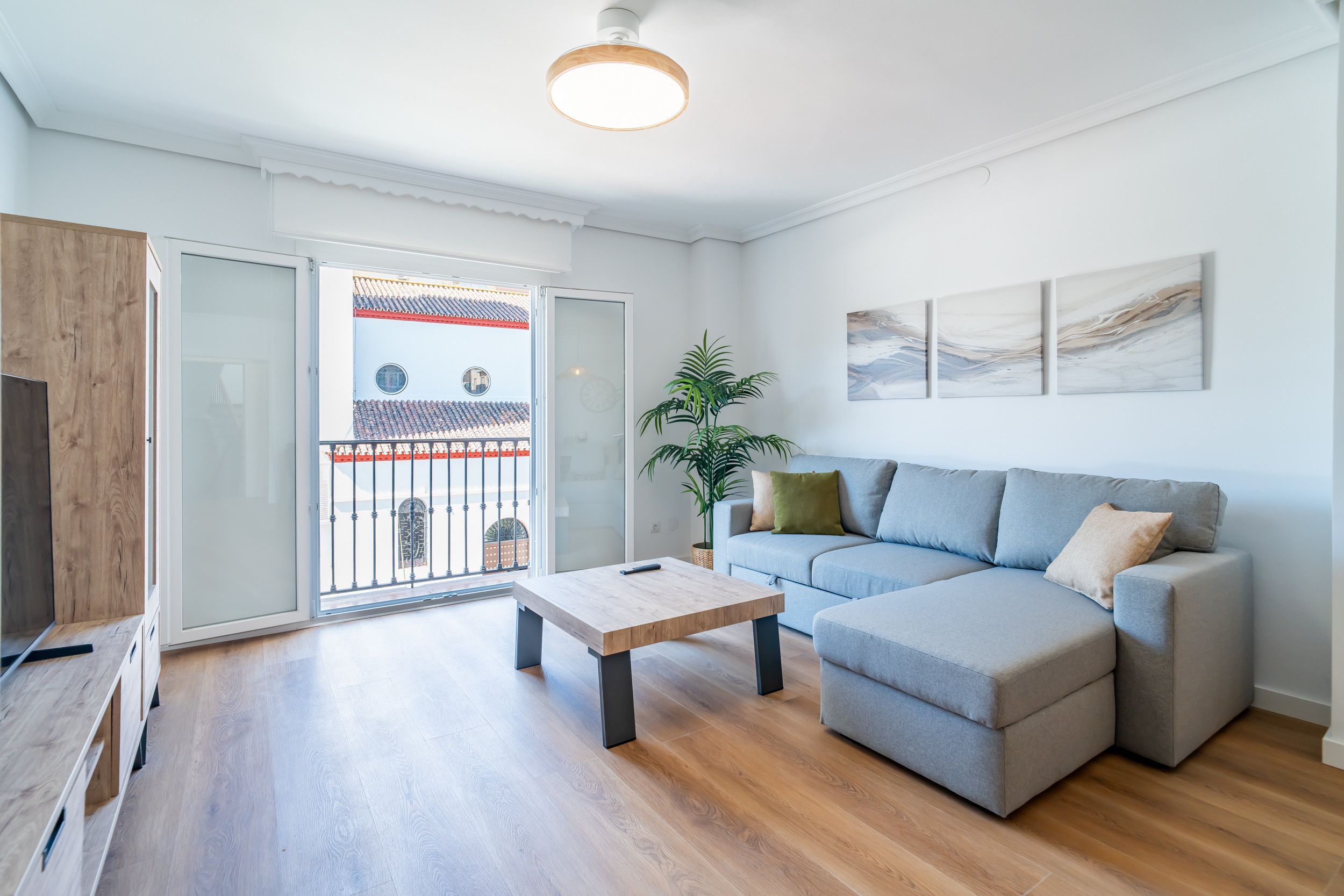 A modern living room with a grey sofa, a wooden coffee table, and a large window with a view of a traditional building.