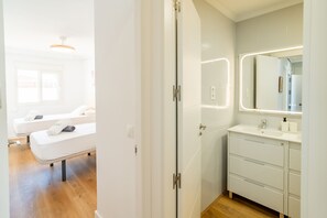 Een moderne badkamer met een grote spiegel, witte kastjes en een houten vloer.