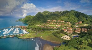 Un resort costero con un puerto deportivo, acceso a la playa y villas en la ladera.