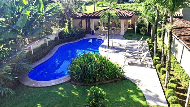 A swimming pool surrounded by a well-maintained lawn, with a patio area and lounge chairs. - 3BR Condo With Pool Near Los Sueños, Herradura (Jacó)