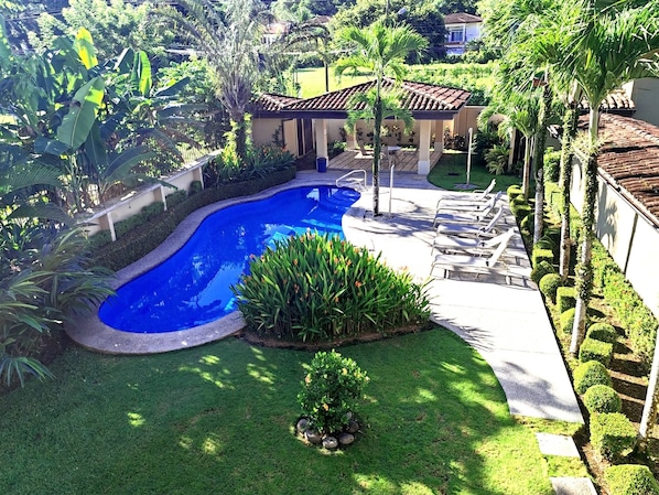 Una piscina rodeada de un césped cuidado, con un área de patio y sillones de descanso.