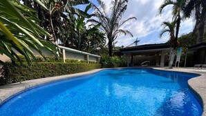A clear blue swimming pool surrounded by tropical plants and a covered area with chairs. - 3BR Condo With Pool Near Los Sueños, Herradura (Jacó)