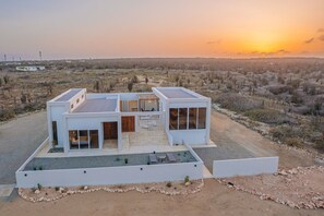 A modern two-story house with a flat roof, large windows, and a patio area. - 3BR Sunrise Villa with Ocean Views and Pool near Baby Beach - Casa Cuadra by Bocobay (Noord)
