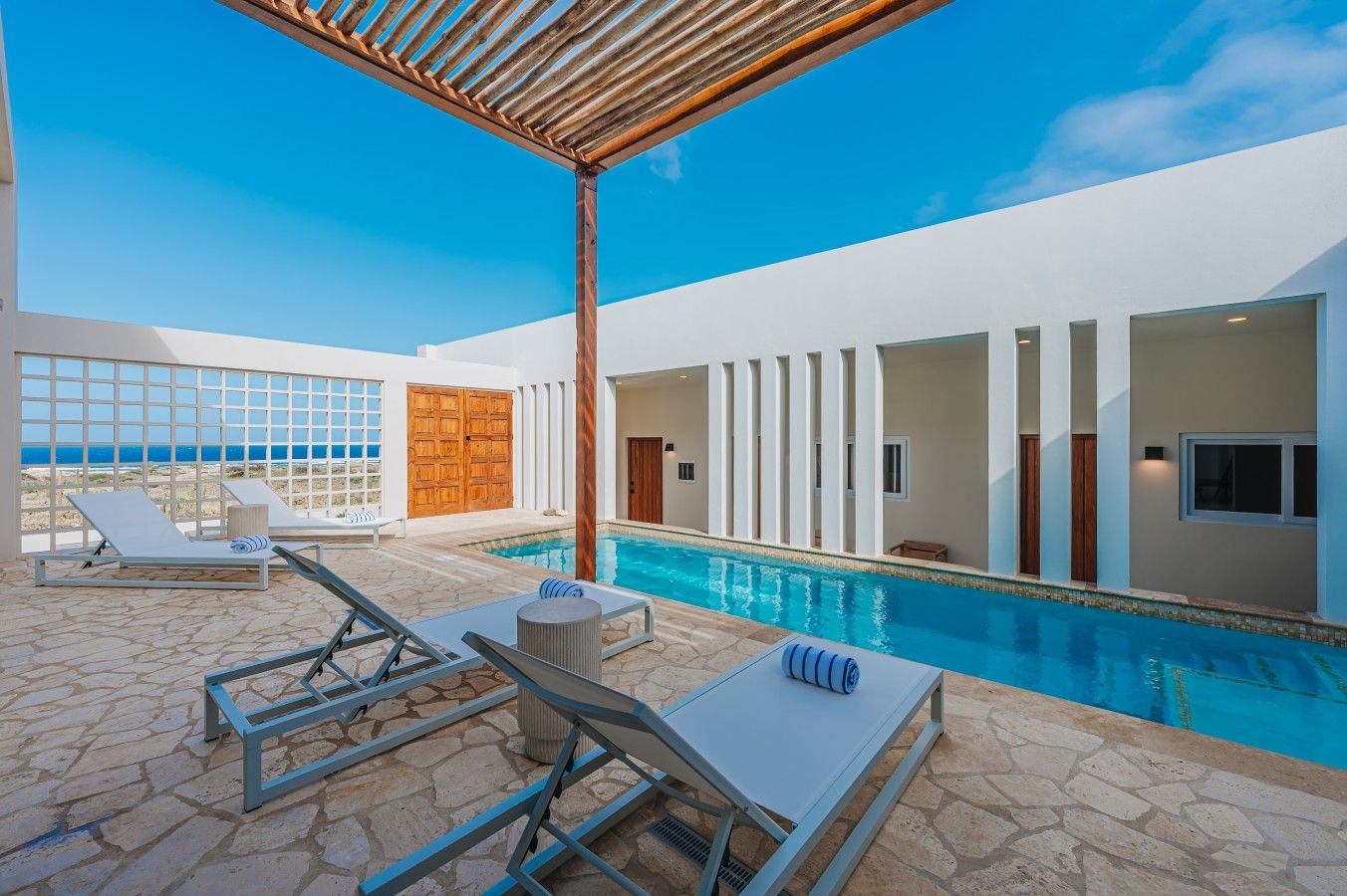 Un espace piscine extérieur moderne, doté de chaises longues et d’une pergola.