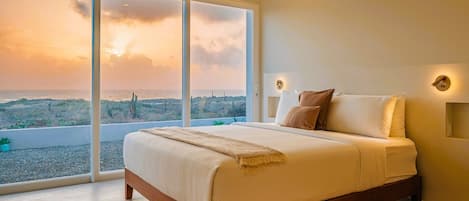 Un dormitorio con una cama grande, vistas a la playa y un ventanal corredero.