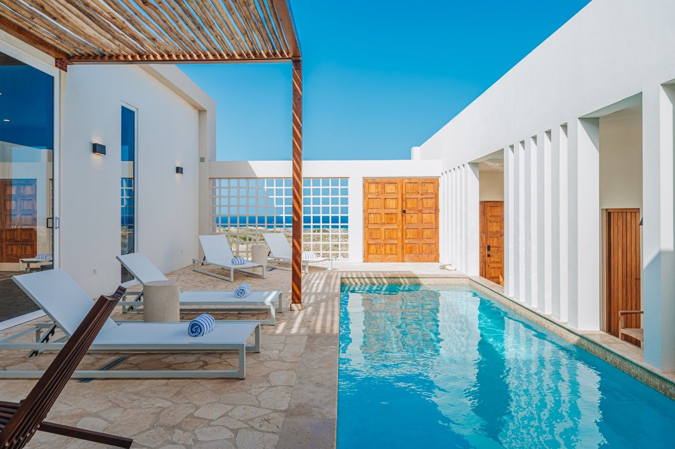 A pool area with lounge chairs, a wooden pergola, and a view of the sea.