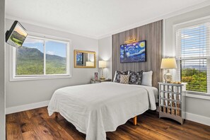 A bedroom with a bed, a bedside table, a lamp, a mirror, and a painting on the wall. - Panoramic Smoky Mountain Views, Indoor Pool, 2 BD (Gatlinburg)