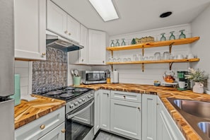 A modern kitchen with white cabinets, a microwave, a stove, and wooden countertops. - Panoramic Smoky Mountain Views, Indoor Pool, 2 BD (Gatlinburg)