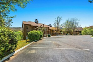 A multi-story building with a parking lot in front, surrounded by greenery and hills in the background. - Panoramic Smoky Mountain Views, Indoor Pool, 2 BD (Gatlinburg)
