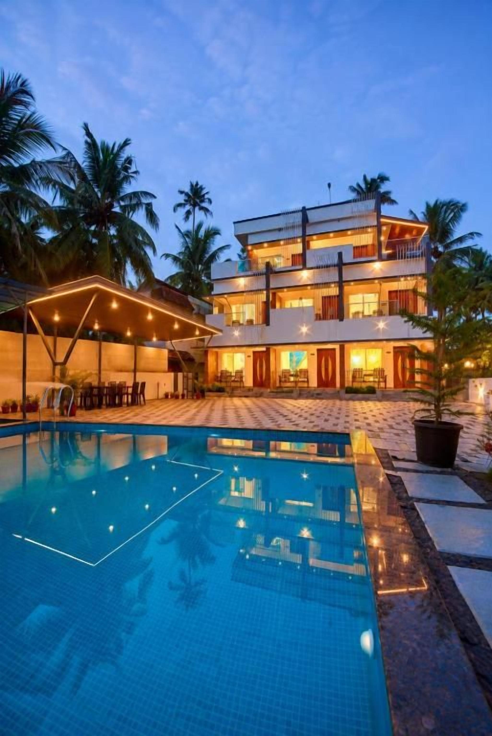 A multi-story hotel with a swimming pool, palm trees, and a well-lit exterior.