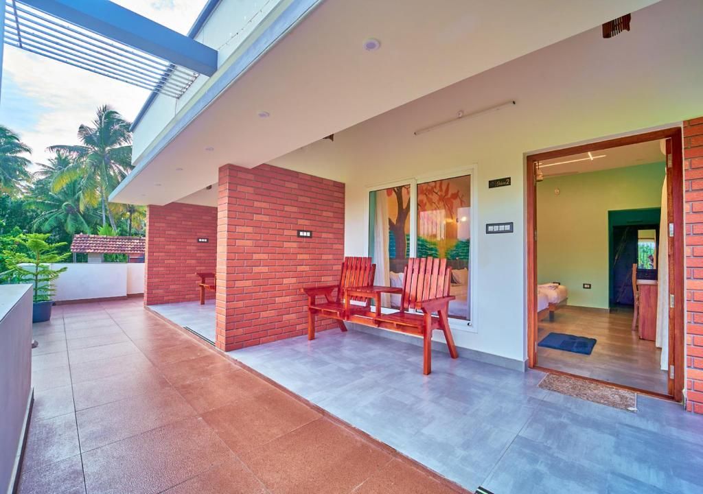 Un área de estar moderna al aire libre con pared de ladrillo, puerta de cristal que da a una habitación y vista a palmeras.