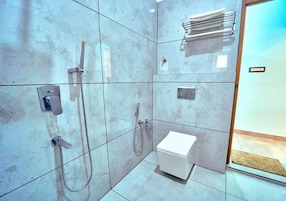 Een moderne badkamer met een wit toilet, een douche met handdouche en een handdoekrek.