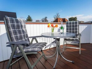 Eine Terrasse mit zwei Stühlen und einem Tisch, einer Weinflasche und einer Vase mit Blumen.