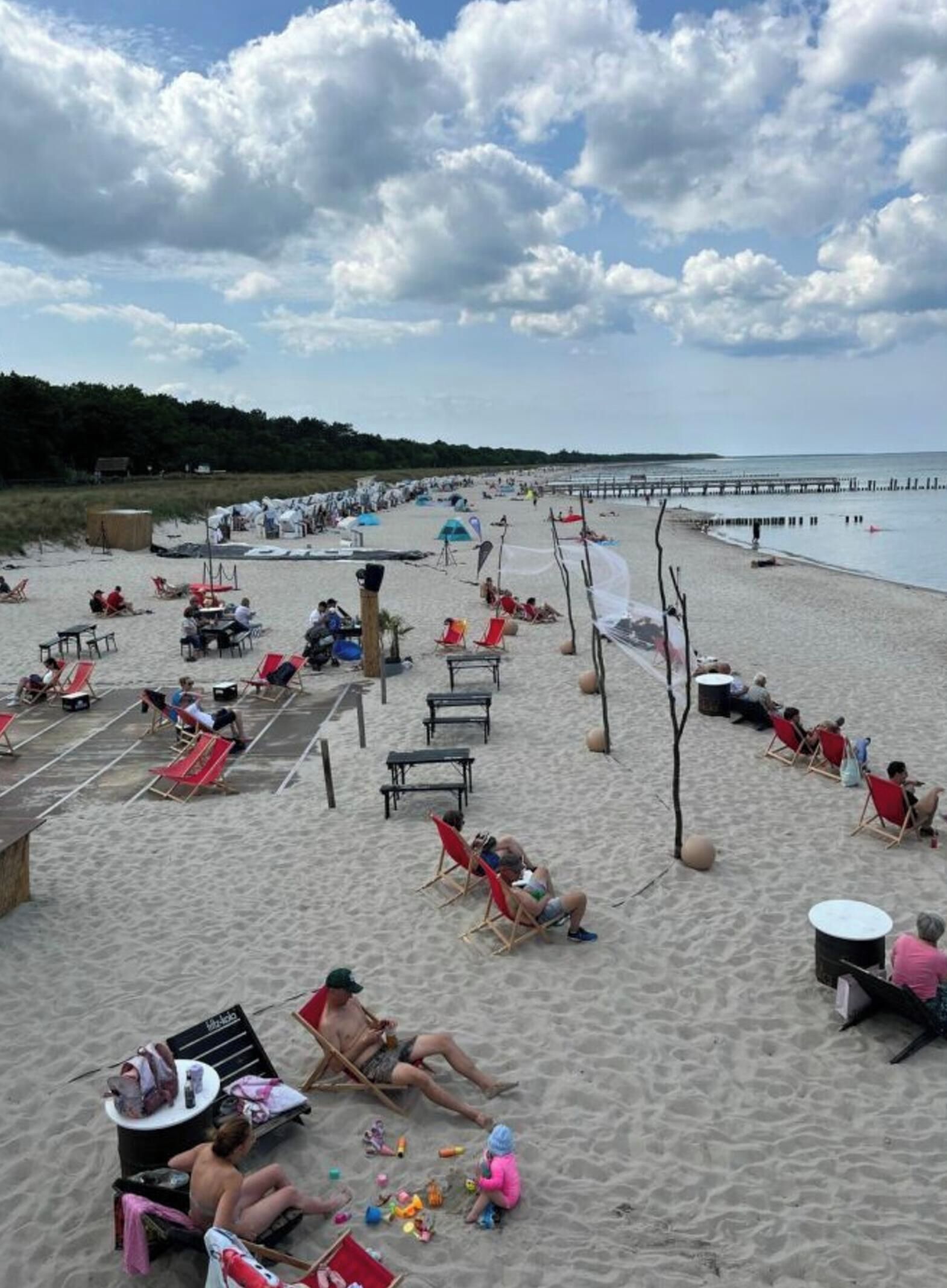 A beach with sun loungers, umbrellas, and a pier extending into the water.
