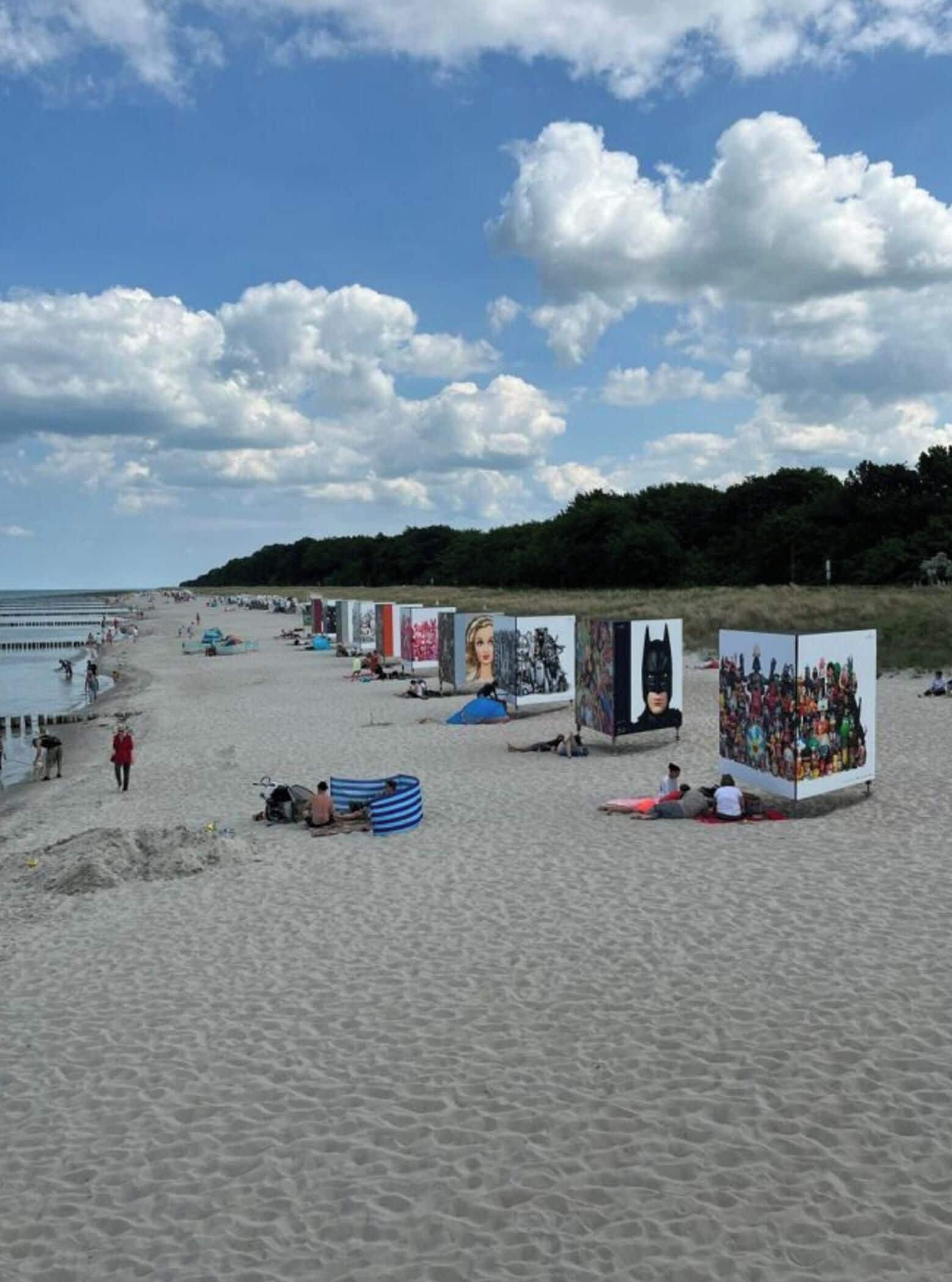 A beach with art installations and people walking.