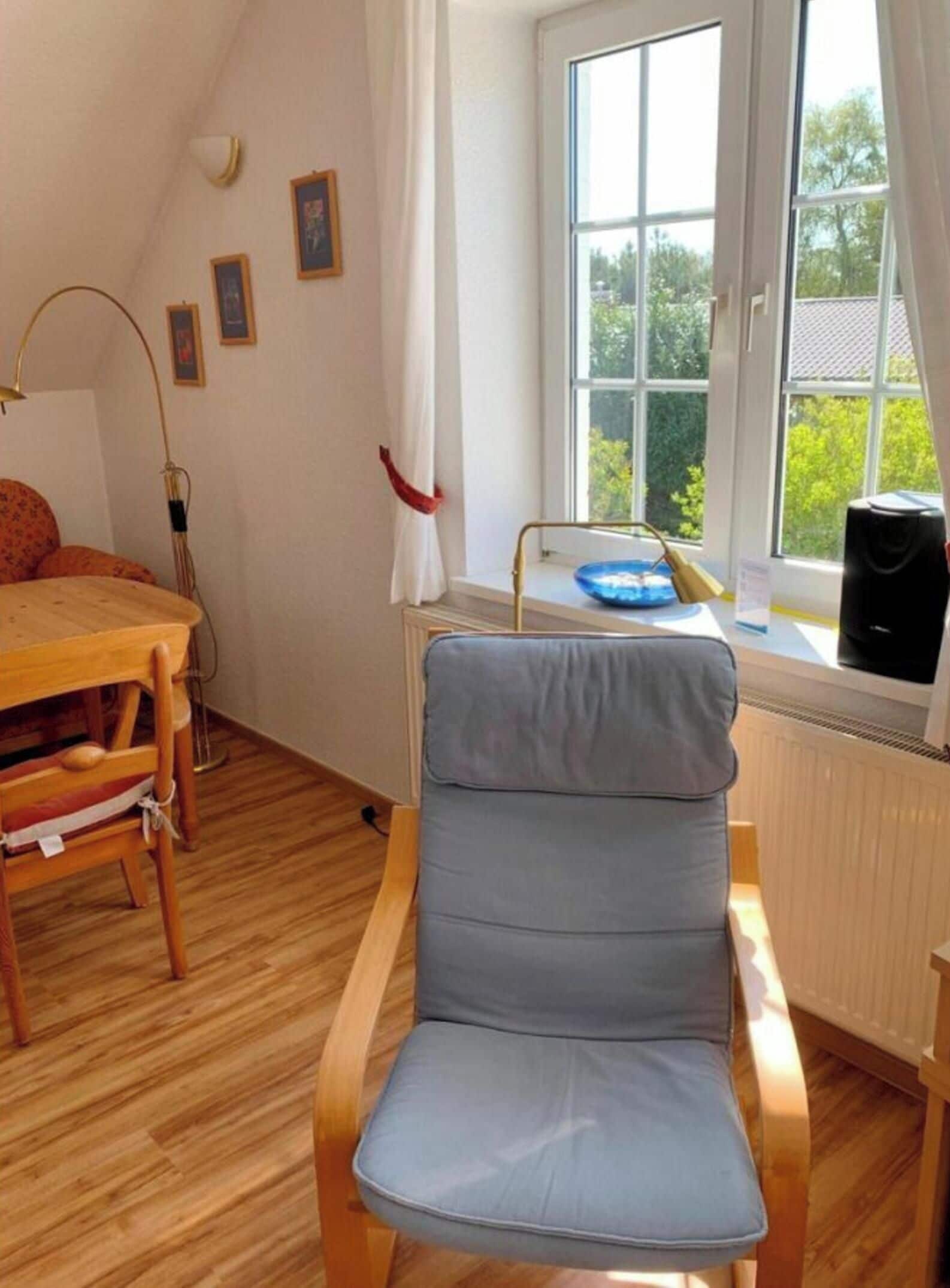 Una habitación con una mesa de comedor de madera, una silla con cojín azul, un radiador y una ventana con vistas a la vegetación.