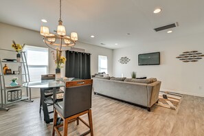 A modern living room with a grey sofa, a dining table with chairs, and a chandelier. - New-build Townhome Near Speedway & Uncc (Charlotte)