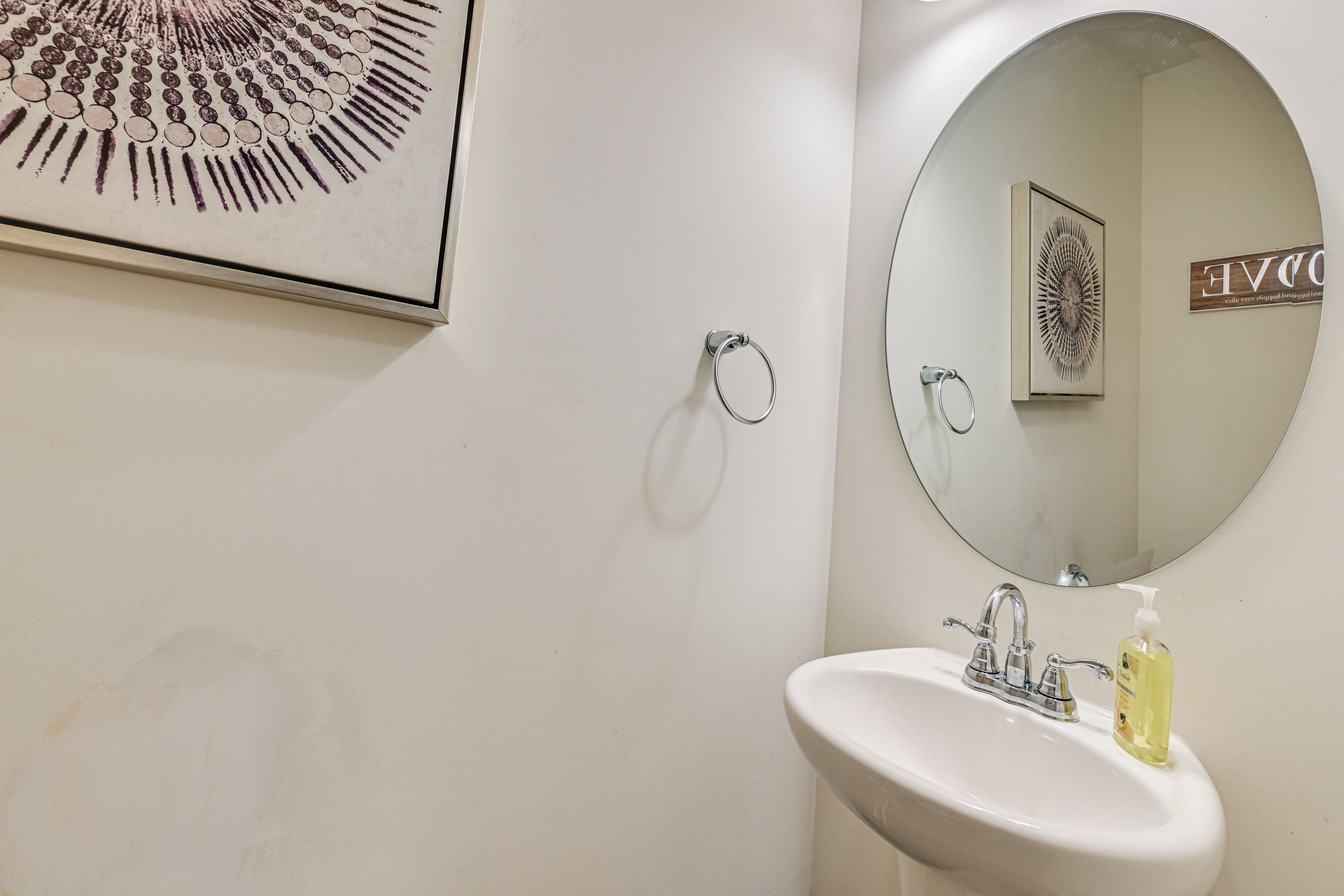 A bathroom with a white sink, a round mirror, and a towel ring.