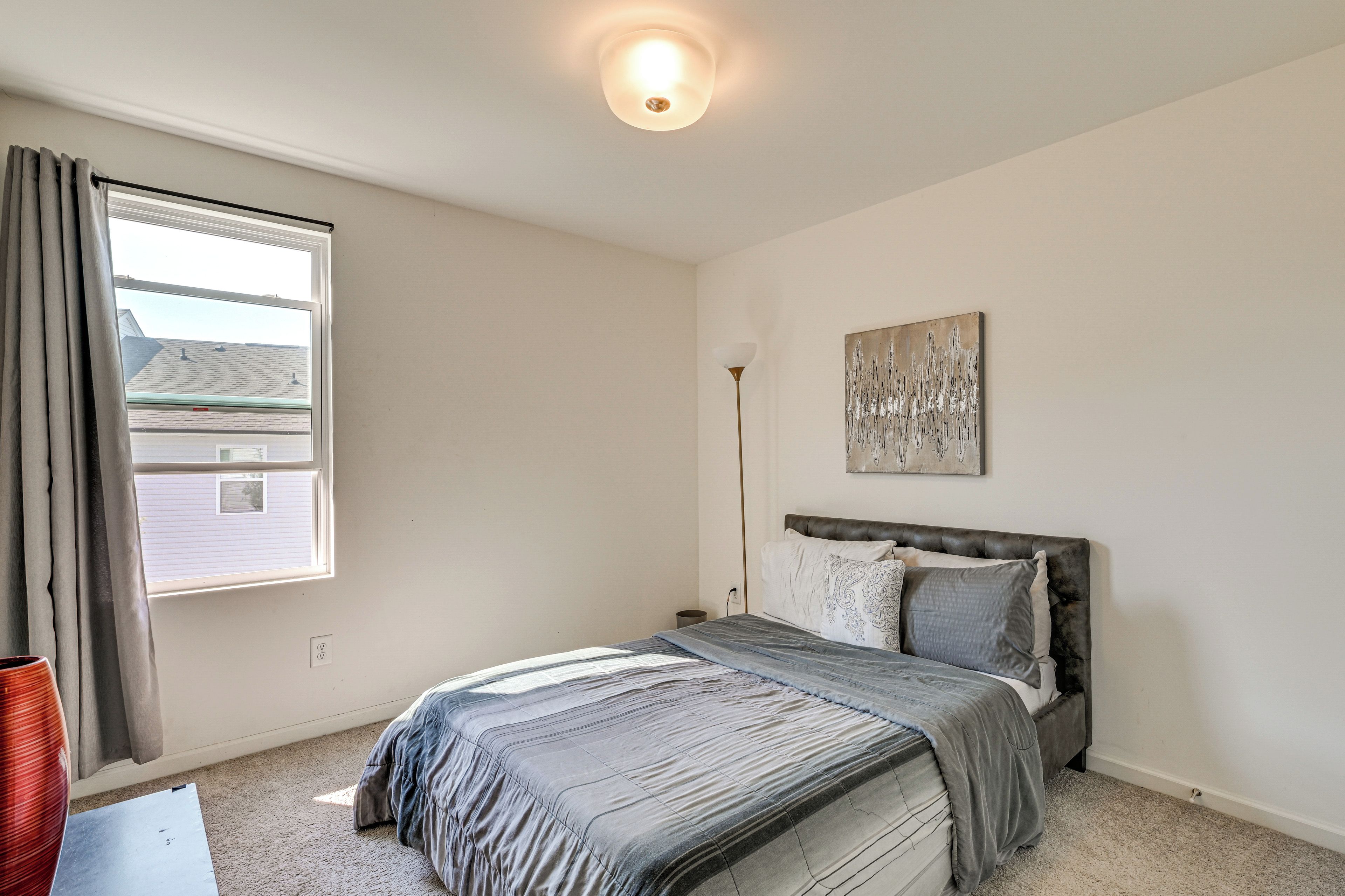 A bedroom with a bed, a window, a floor lamp, and a painting on the wall.
