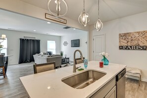 A modern kitchen with a central island, stainless steel sink, and pendant lighting. - New-build Townhome Near Speedway & Uncc (Charlotte)