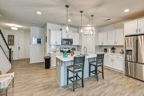 A modern kitchen with white cabinetry, stainless steel appliances, and a central island with two bar stools. - New-build Townhome Near Speedway & Uncc (Charlotte)